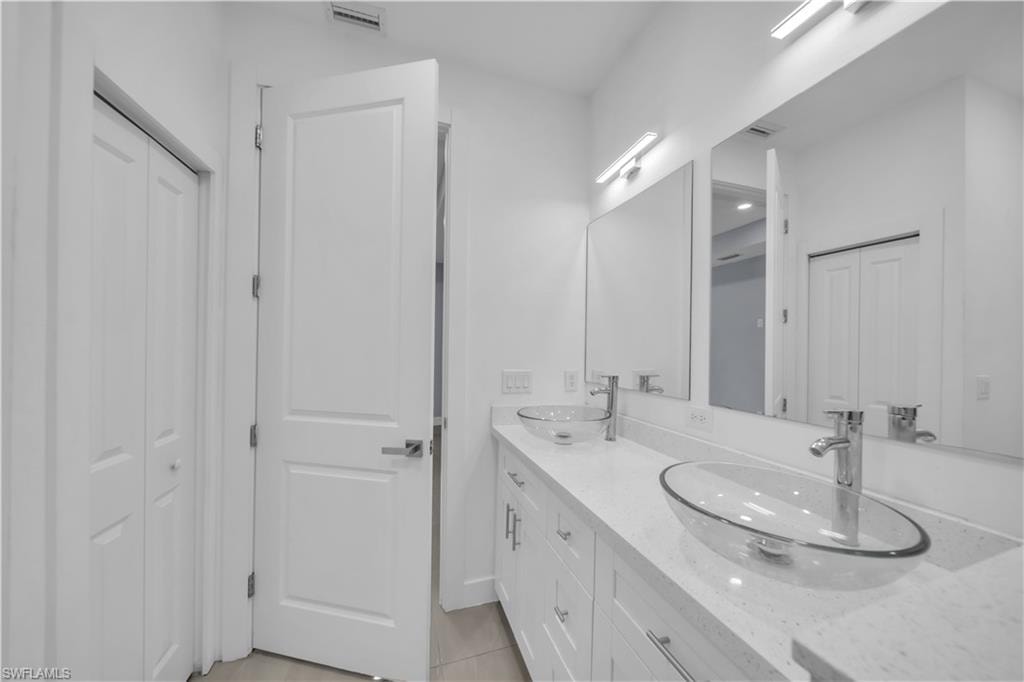 Dual vessel sinks set on a white countertop with integrated cabinetry, illuminated by wall-mounted light fixtures