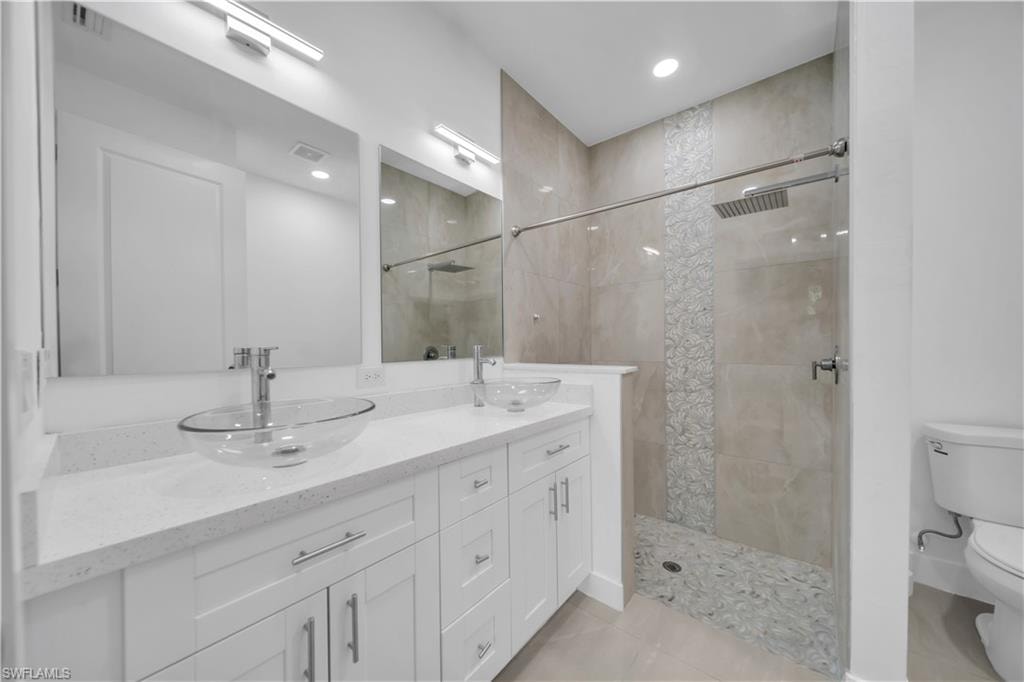 Double vanity with clear vessel sinks, white cabinetry, quartz-finish countertop, and a walk-in shower with a glass enclosure and textured tile accent