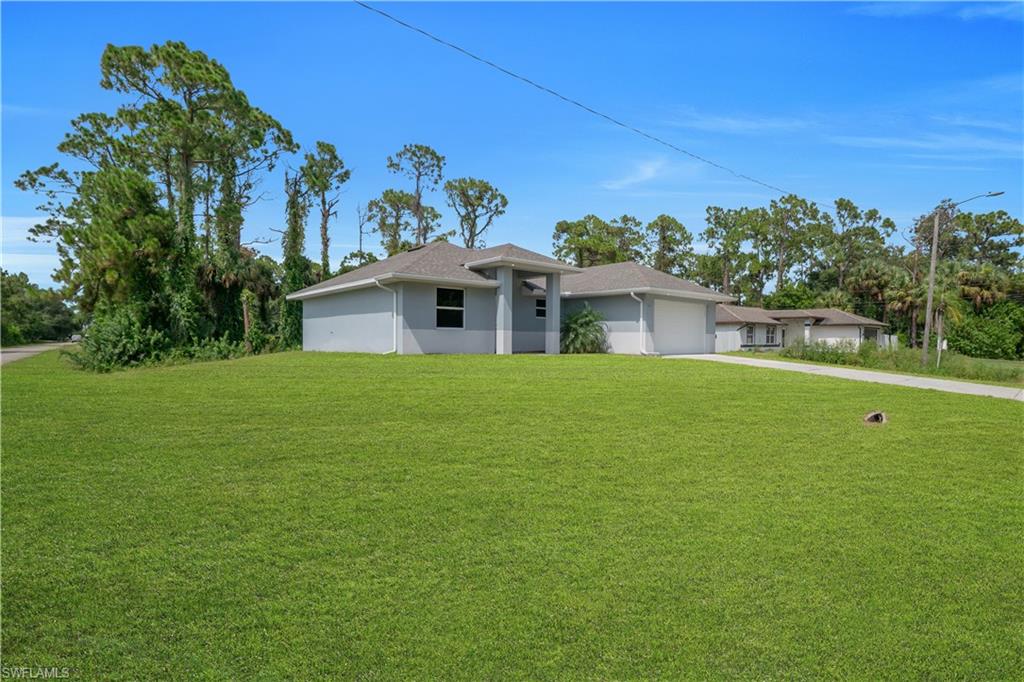 Expansive green lawn, light-colored exterior, attached garage, paved driveway, mature trees
