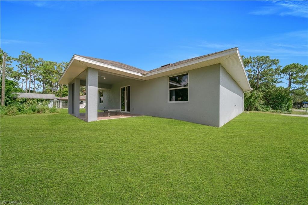 Expansive rear lawn with a covered patio featuring a concrete slab and support columns
