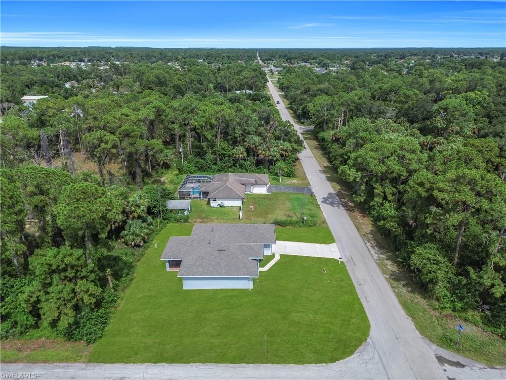 Expansive treed landscape featuring a residential property with a green lawn and a paved driveway