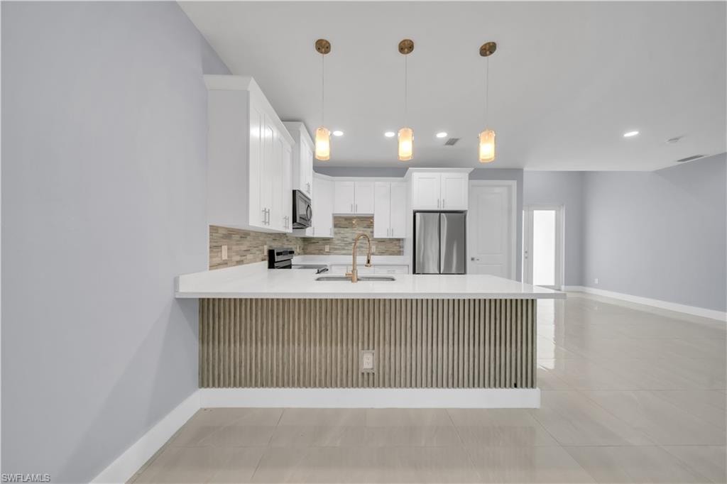 Kitchen featuring white cabinetry, a large center island with a white countertop, stainless steel appliances, and a tiled backsplash
