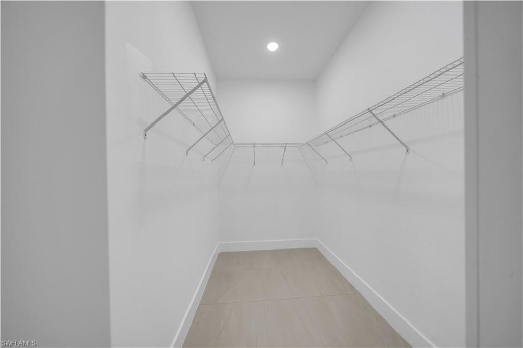 Spacious walk-in closet with white wire shelving, tiled flooring, and recessed lighting