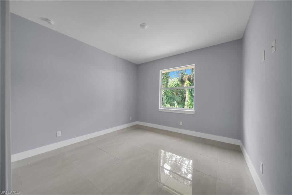 Spacious room featuring light gray walls, large format tile flooring, a window with white trim, and recessed ceiling lighting