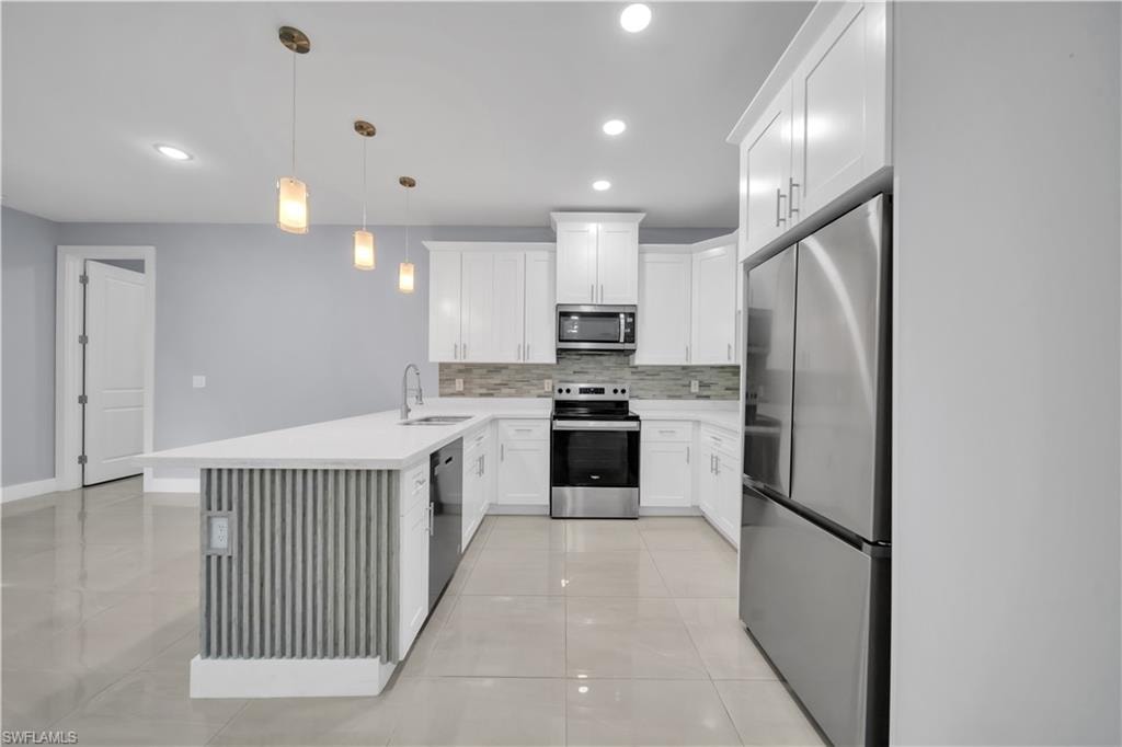 Kitchen with white cabinetry, stainless steel appliances, a center island featuring a sink, and pendant lighting