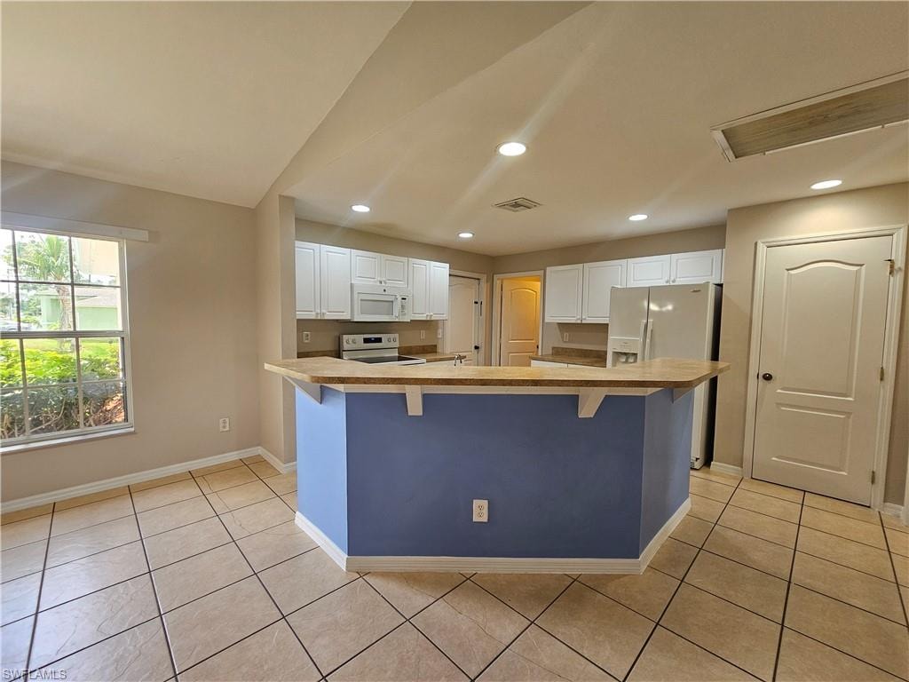 Open-concept kitchen with white cabinetry, light-colored countertops, recessed lighting, and tile flooring