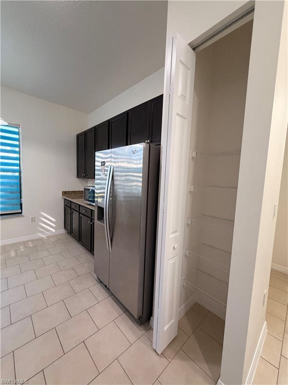 Kitchen featuring stainless steel refrigerator, dark wood-finish cabinetry, patterned backsplash, and light tile flooring