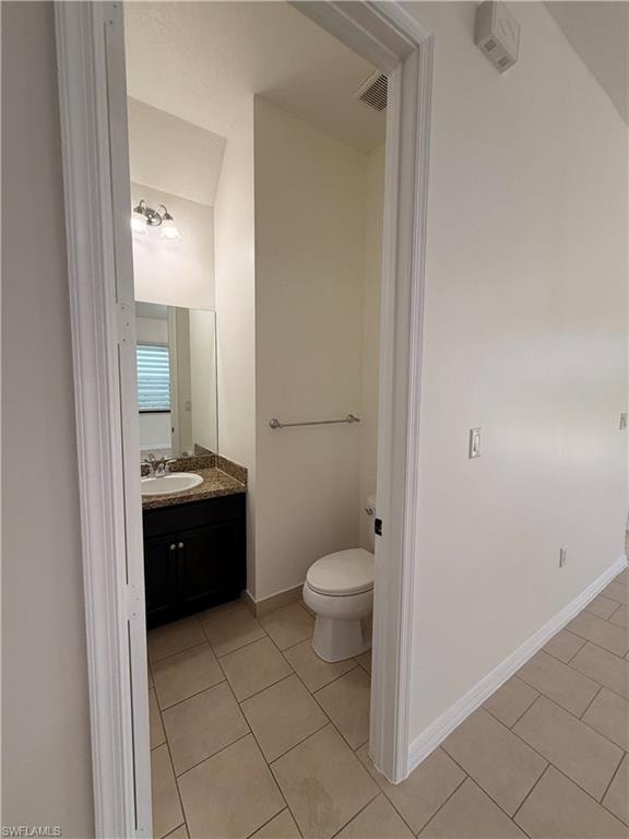 Tile flooring, dark wood-finish vanity, granite countertop, wall-mounted mirror, and white toilet