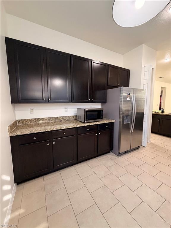 Dark wood-finish cabinetry, light-toned tiled flooring, stone-finish countertops, and stainless steel refrigerator