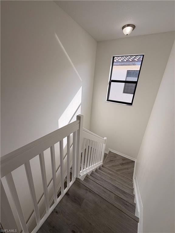 Staircase featuring wood-finish flooring, white painted railings, a window with black trim, and a flush-mount ceiling light
