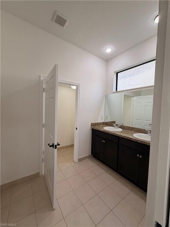 Dual vanity with under-mount sinks, granite countertop, dark wood-finish cabinetry, and tiled flooring