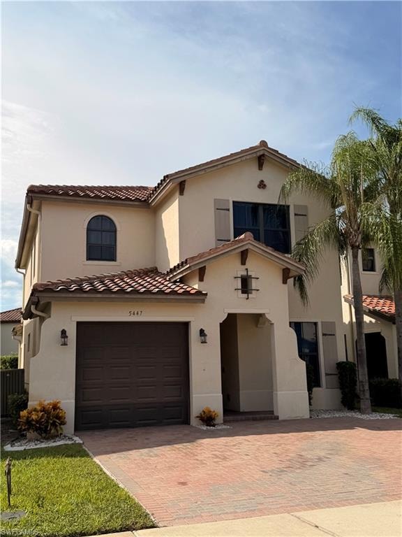 Stucco exterior with a tile roof, arched entryway, and a brick paver driveway