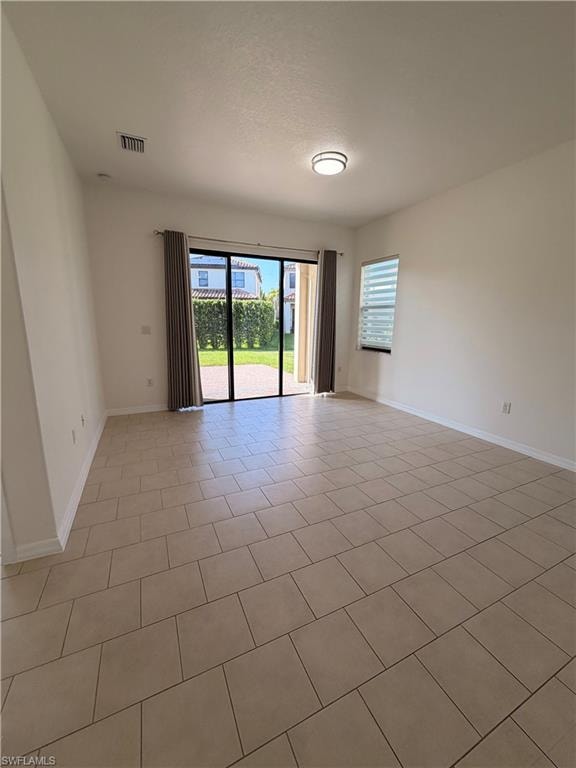 Neutral tone tile flooring, sliding glass patio doors, window with blinds, flush-mount ceiling light fixture