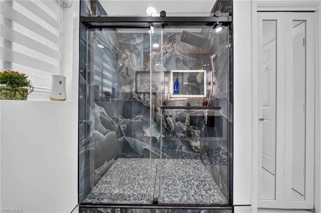 Glass-enclosed shower with dark-toned, veined wall panels and a pebble-finish floor