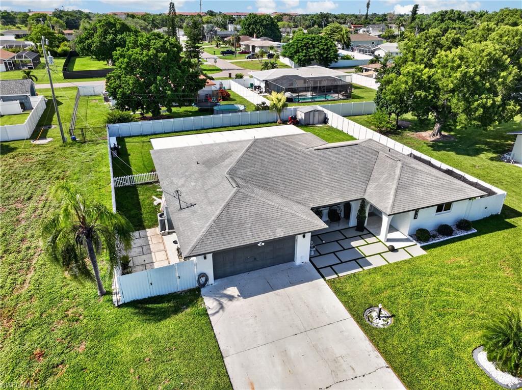 Expansive concrete driveway, attached two-car garage, contemporary gray shingle roof, white privacy fencing, and geometric concrete paver walkway