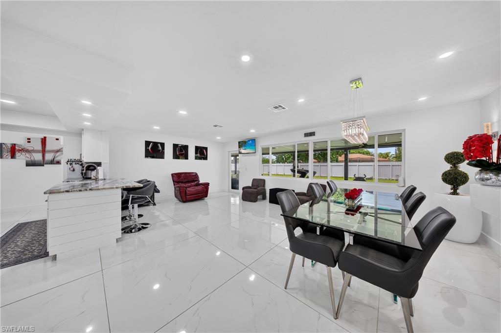 Recessed lighting illuminates an open living area featuring large format tile flooring, a kitchen island with a stone countertop, and an array of large windows