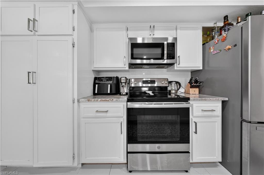 White cabinetry with brushed nickel hardware, stainless steel appliances, granite-style countertops, and a subway tile backsplash