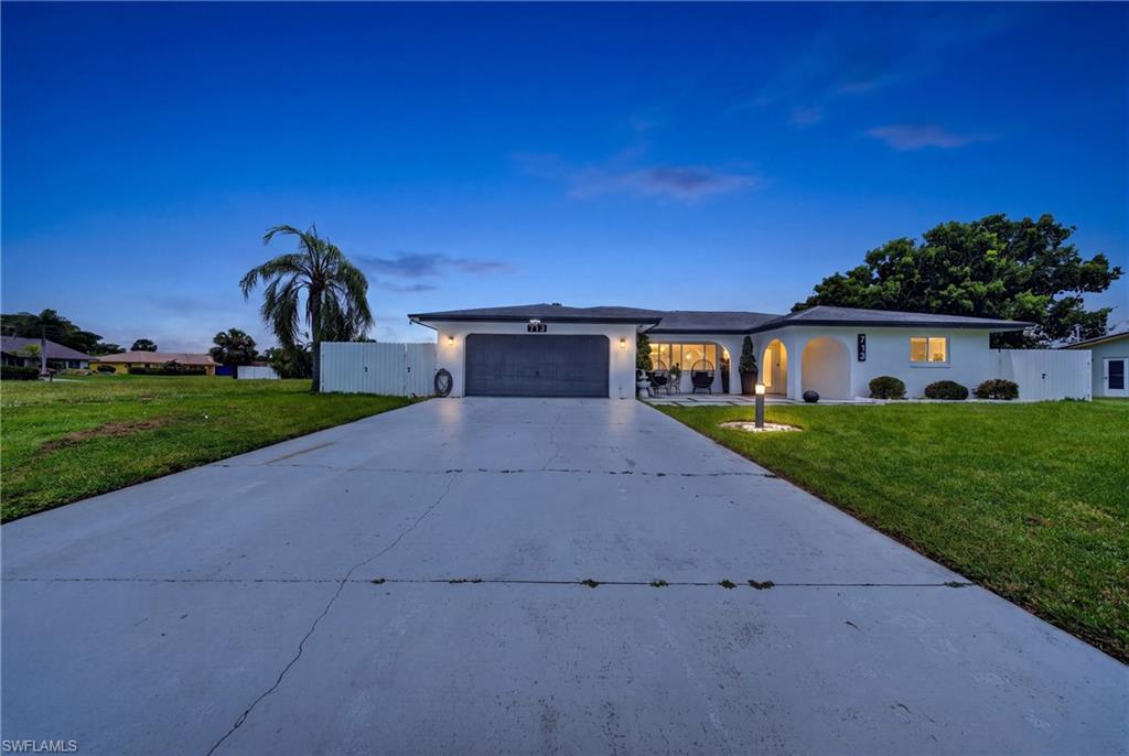 Stucco exterior with arched entryway, attached two-car garage, concrete driveway, and manicured lawn