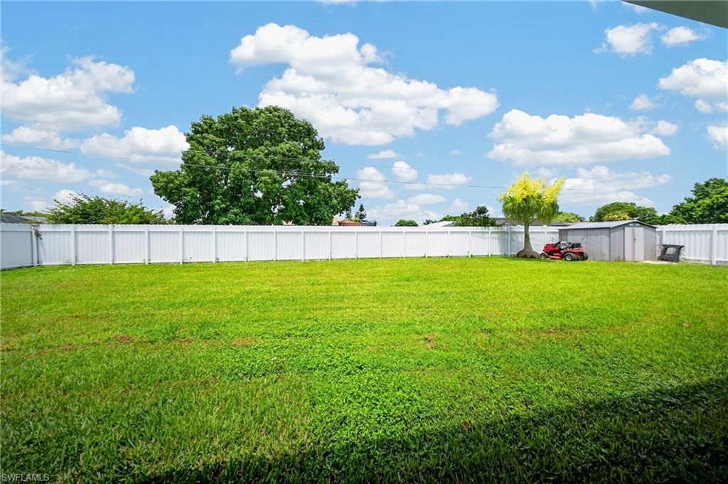 Expansive lawn area featuring a full perimeter white privacy fence, mature trees, and a metal storage shed