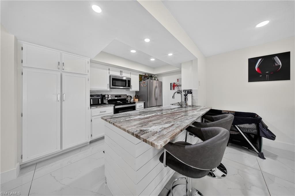 Kitchen featuring a multi-tone island countertop, stainless steel appliances, white cabinetry, and recessed lighting