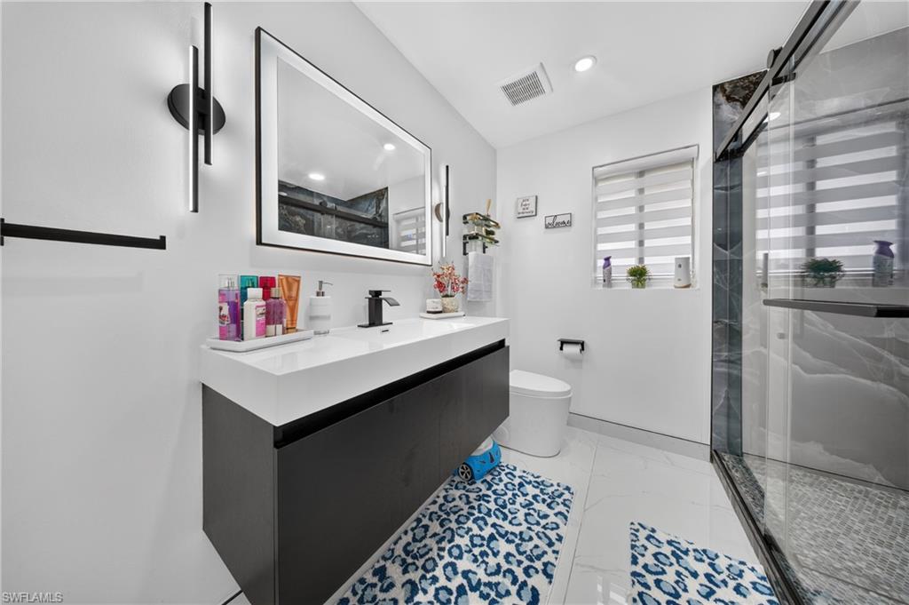 Floating vanity with integrated sink, black framed mirror, walk-in shower with glass enclosure, tiled shower walls, and white tiled flooring