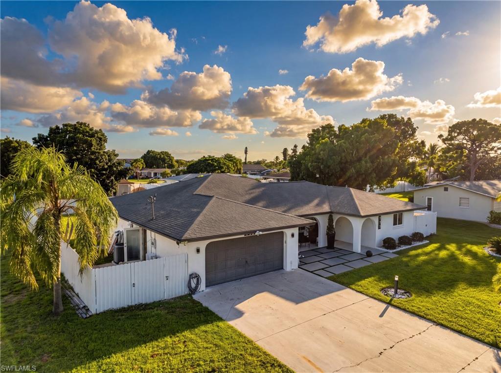White exterior with dark gray roof, two-car garage, arched entry, and manicured green landscaping