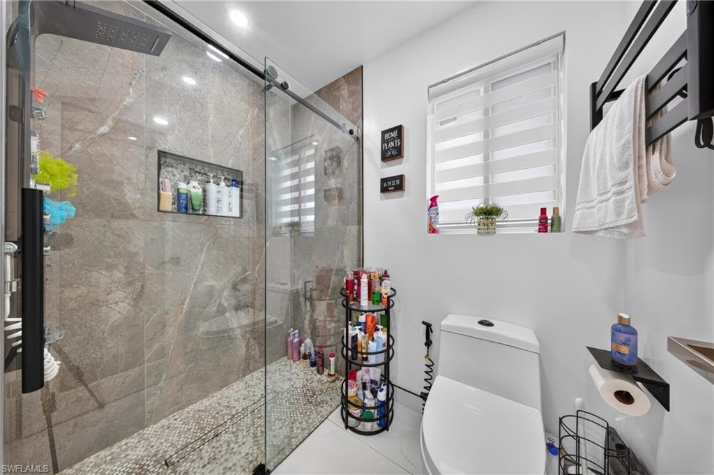 Glass-enclosed shower with stone-finish wall tile, pebble-style flooring, and a built-in shower niche