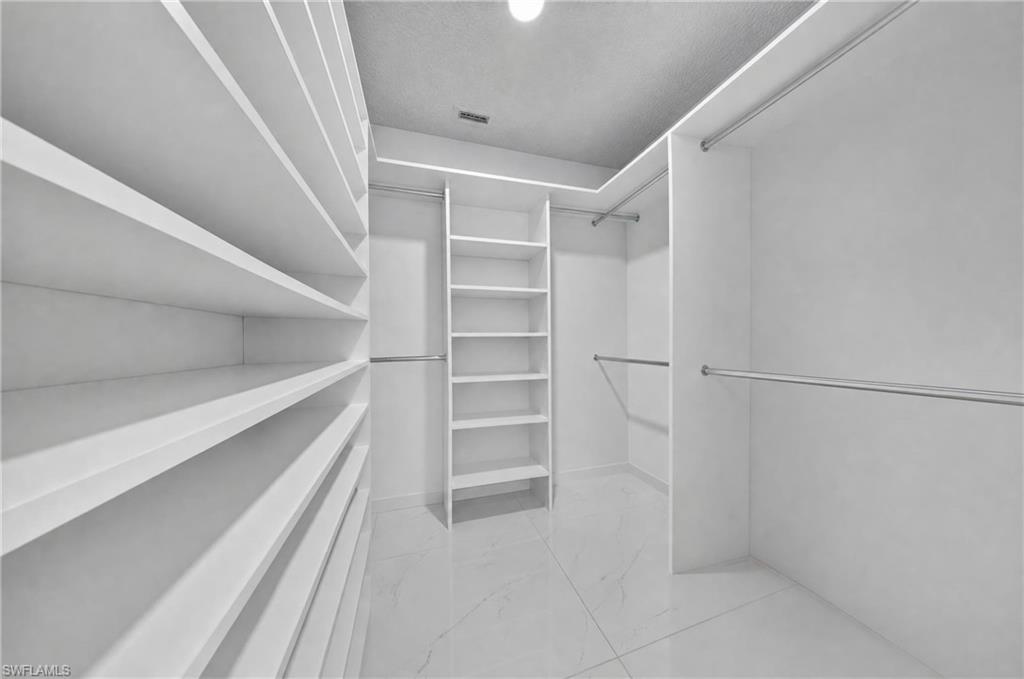 Walk-in closet with extensive built-in shelving, multiple hanging rods, corner shelving unit, and tile flooring