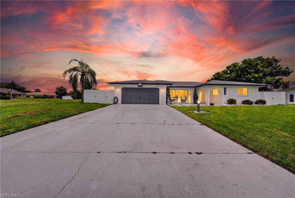 Expansive concrete driveway, attached two-car garage, white exterior finish, arched entryway, and a manicured front lawn