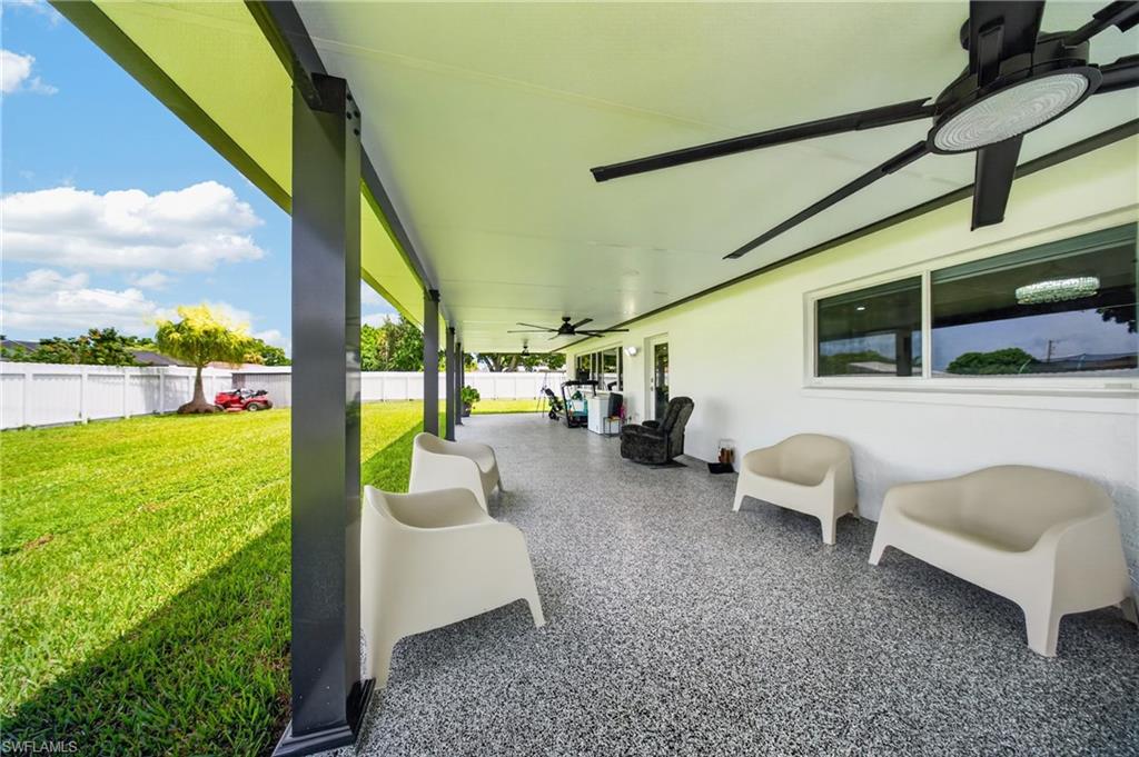 Covered patio with a speckled concrete finish, overhead ceiling fans, and a white privacy fence enclosing a grassy yard
