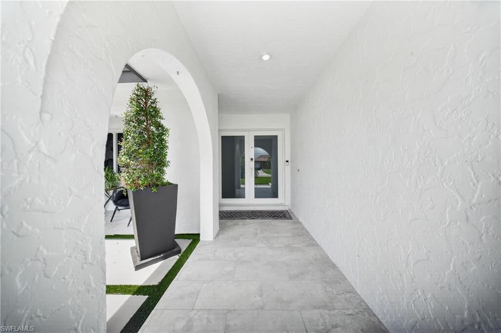Arched entryway with a textured white stucco finish, recessed lighting, and light-toned tile flooring