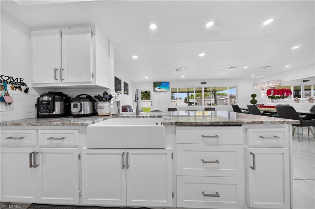 White shaker cabinetry with modern hardware, farmhouse sink, integrated lighting, and granite-style countertops