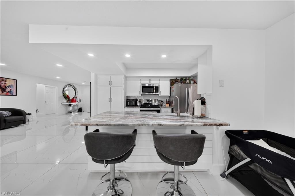 Modern kitchen island with a stone-finish countertop, white shaker-style cabinetry, stainless steel appliances, and white tile flooring