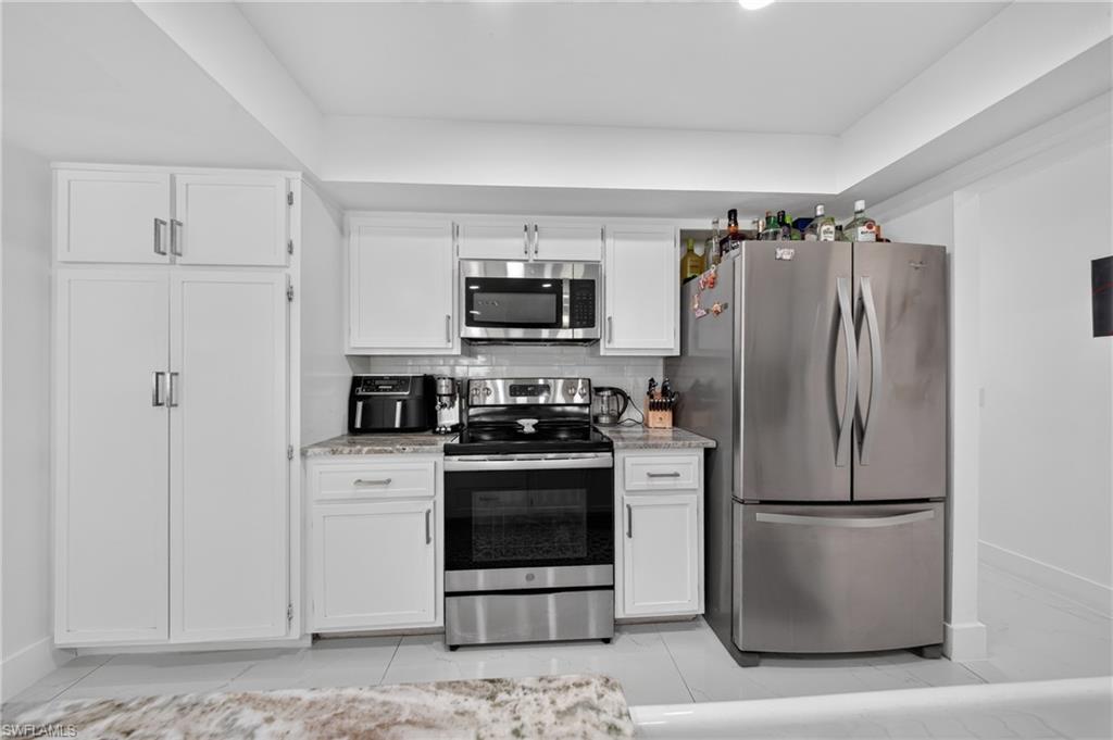 White cabinetry, stainless steel appliances, subway tile backsplash, and light-toned countertops