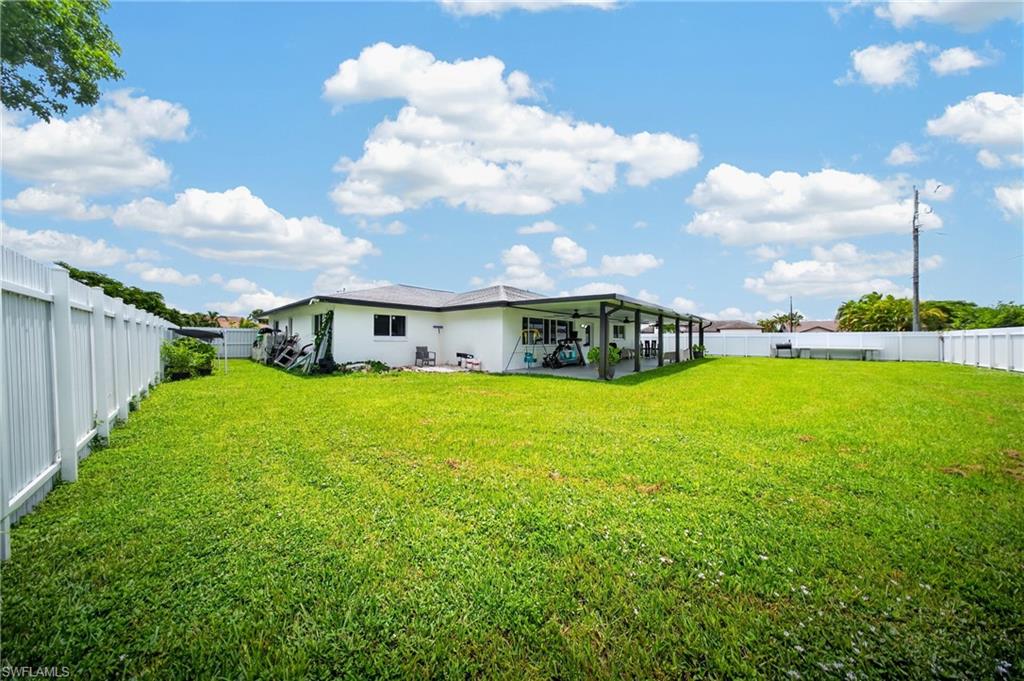 Expansive green lawn, white perimeter fencing, and a covered patio area