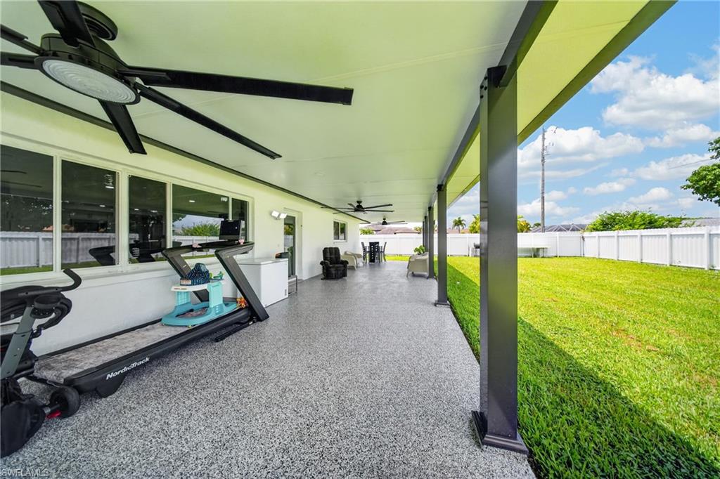 Expansive covered patio with a speckled finish floor, multiple ceiling fans, and a partial white privacy fence