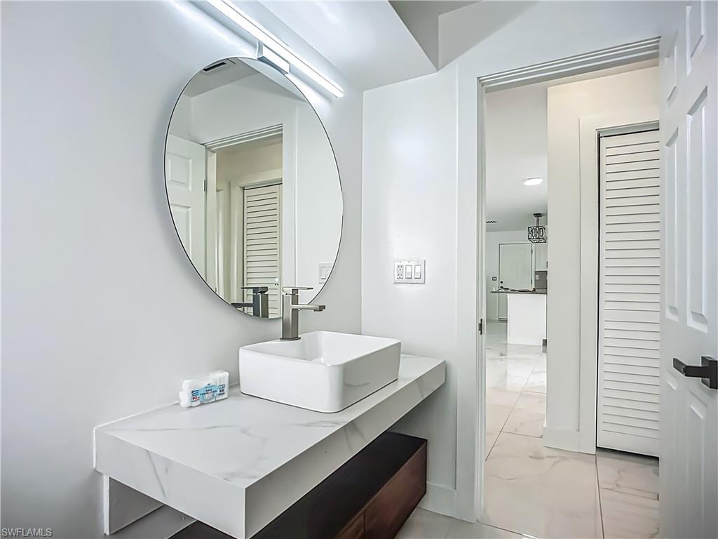 Floating vanity with a white rectangular vessel sink, marble-patterned countertop, and circular mirror