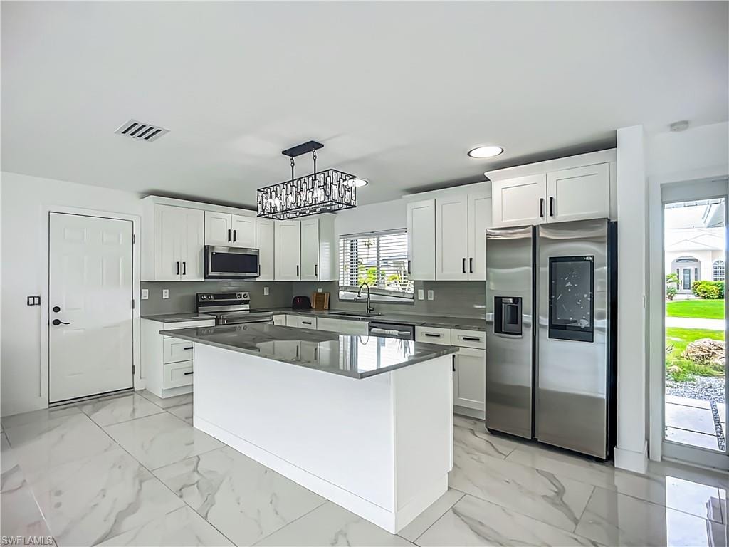 Kitchen featuring a center island, white cabinetry, stainless steel appliances, and large format tile flooring