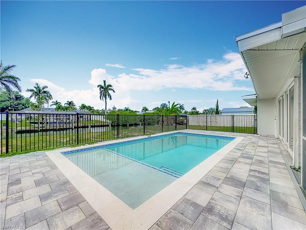 Paved patio with a rectangular swimming pool, surrounded by a black metal fence