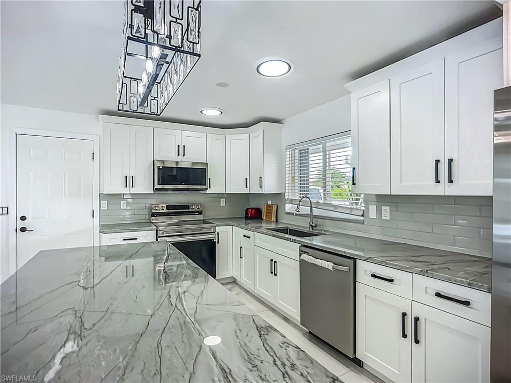 Kitchen featuring white shaker cabinetry, stainless steel appliances, grey subway tile backsplash, and a large island with a patterned countertop