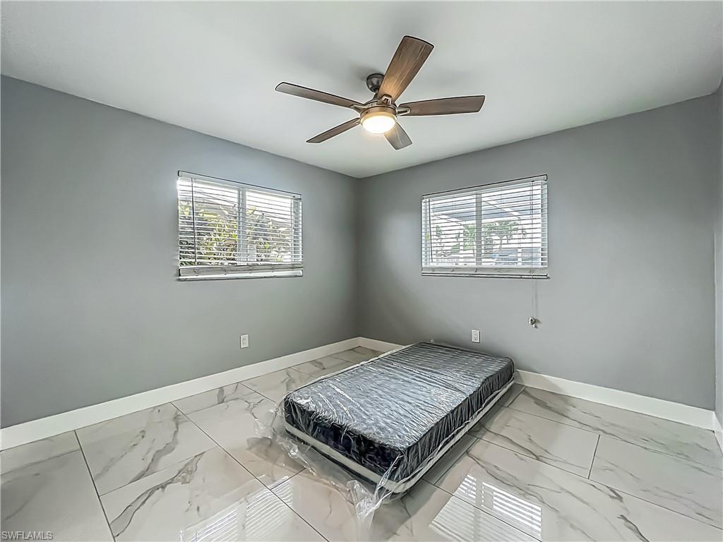 Rectangular room featuring two windows with horizontal blinds, a ceiling fan with integrated lighting, and large format tile flooring