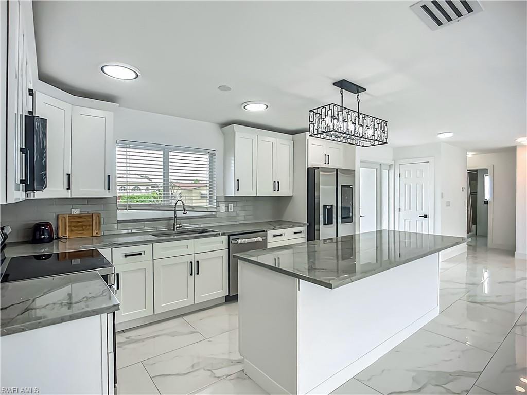 White shaker cabinetry, stainless steel appliances, grey subway tile backsplash, white tile flooring, and a stone-finish island countertop