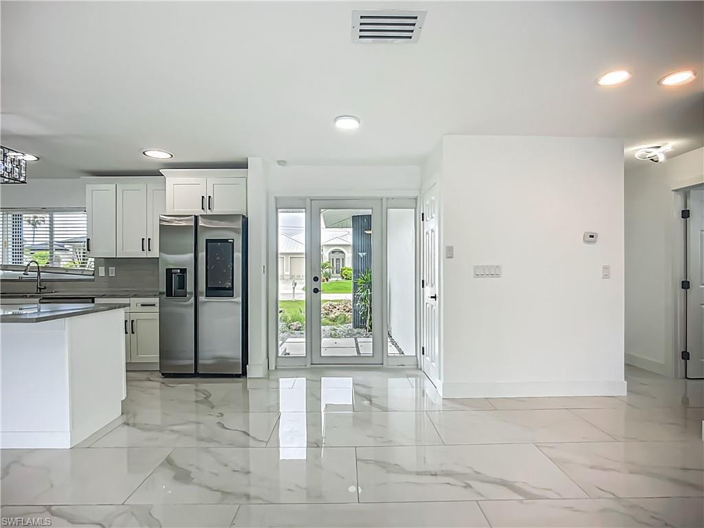 Modern kitchen with white cabinetry, stainless steel refrigerator, and light-toned backsplash