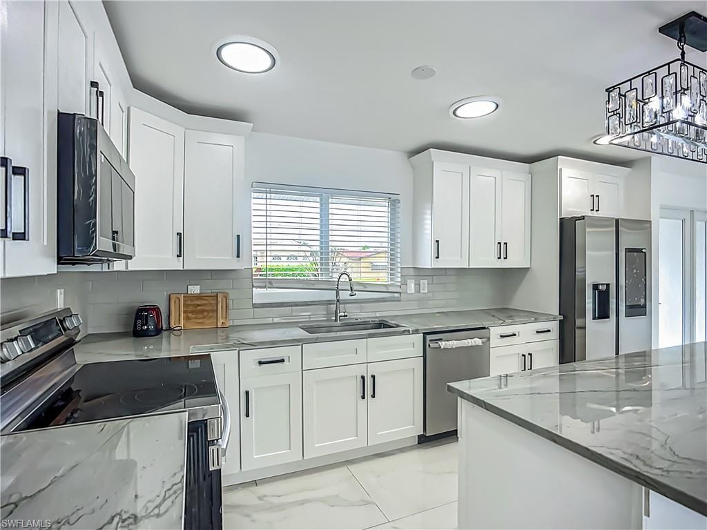 White shaker cabinetry with black hardware, stainless steel appliances, gray subway tile backsplash, recessed lighting, and a kitchen island with a stone-finish countertop