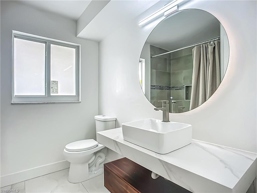 Floating vanity with a rectangular vessel sink, a backlit round mirror, and a shower with tiled walls