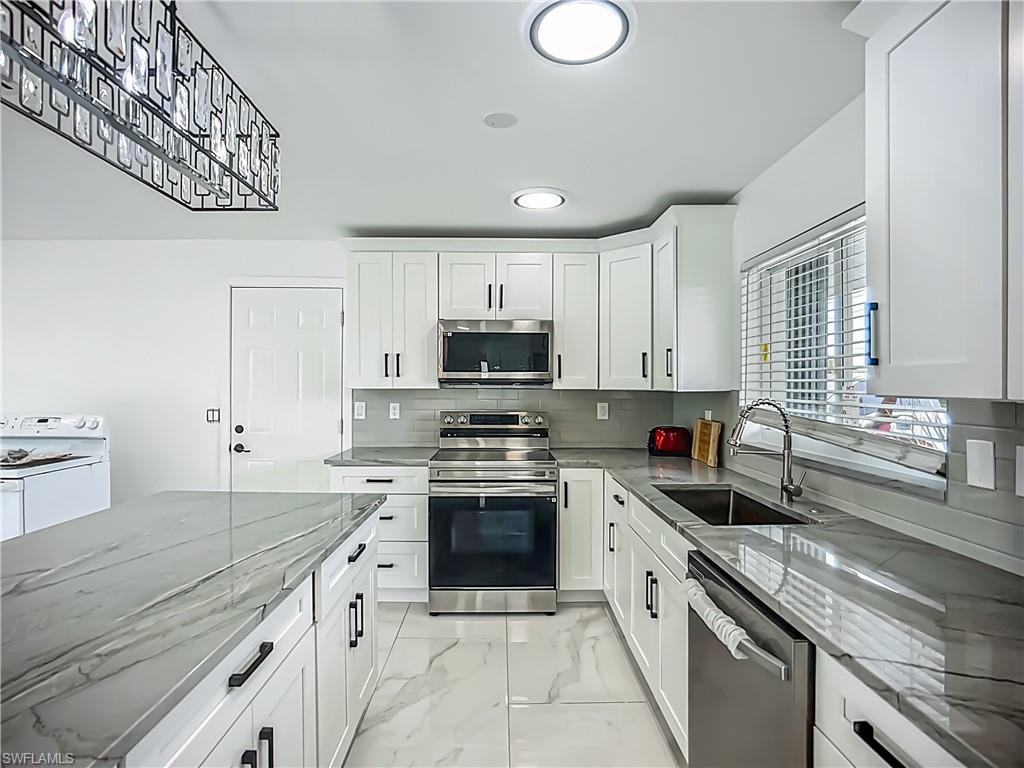 White shaker cabinetry with black hardware, stainless steel appliances, grey veined countertops, grey subway tile backsplash, and recessed lighting