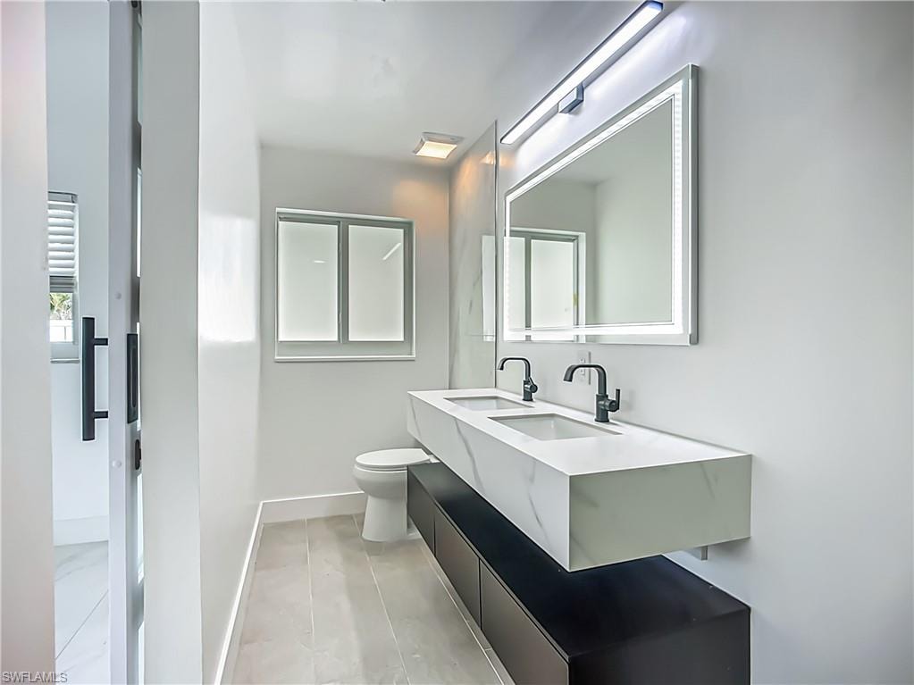 Floating double vanity with integrated sinks, black matte hardware, illuminated mirror, and contemporary tile flooring