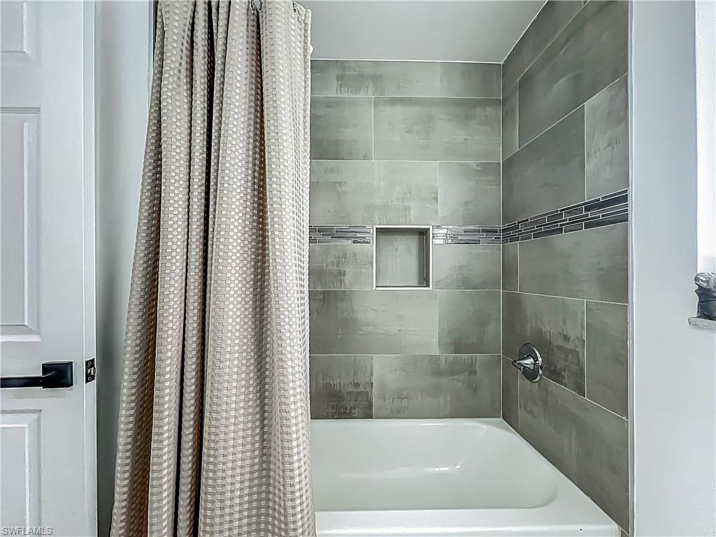 Bathtub with tiled surround, recessed shower niche, decorative tile accent band, and chrome fixtures