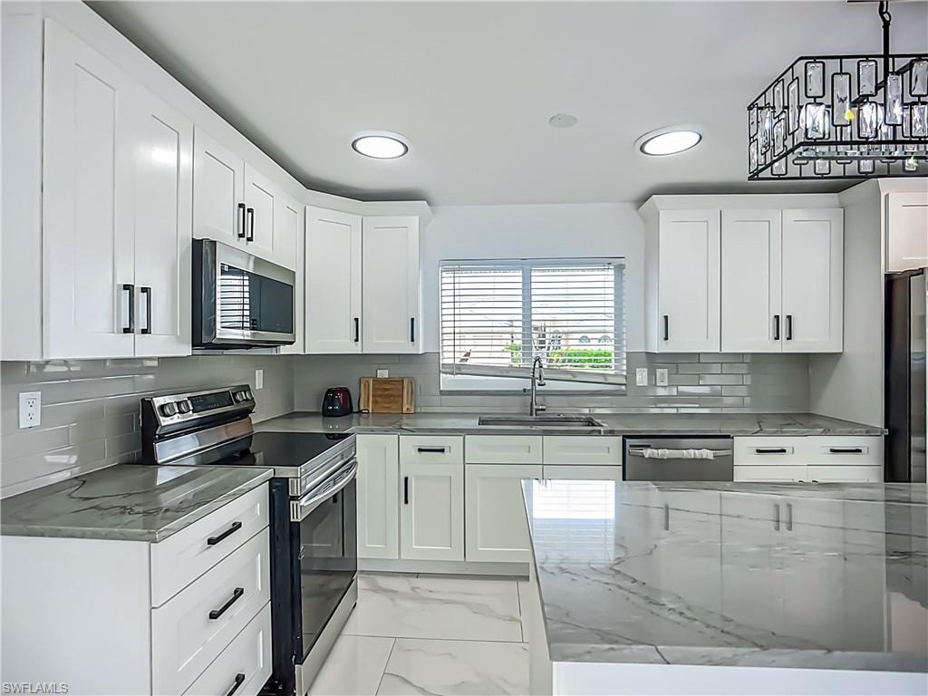 White shaker cabinetry, grey subway tile backsplash, stainless steel appliances, large kitchen island with a waterfall countertop, and recessed lighting