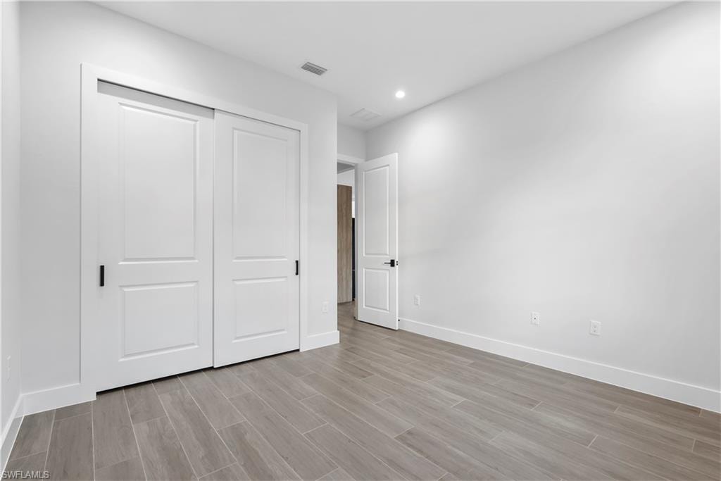 Recessed lighting, wood-finish flooring, white walls, white two-panel sliding closet doors with black hardware, and a white two-panel door with black hardware